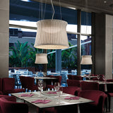 Syra 60 Aluminium LED Outdoor Pendant Light with woven ivory drum shade, shown above burgundy chairs in a restaurant dining area near large windows.