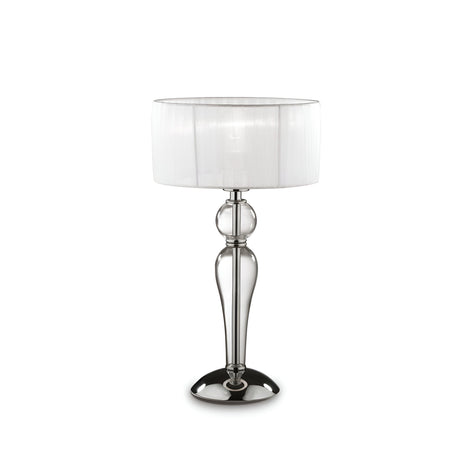 The Arclumis Small Table Lamp - Clear features a transparent glass base with a chrome finish, accompanied by its cylindrical design. It is topped with a white fabric drum-shaped lampshade, offering a modern and sophisticated look. The lamp is turned off.