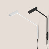 Nivia LED wall light with reading light in matt white, shown beside a black version, each with angled arm, cylindrical head and wall-mounted switch plate on a plain background.