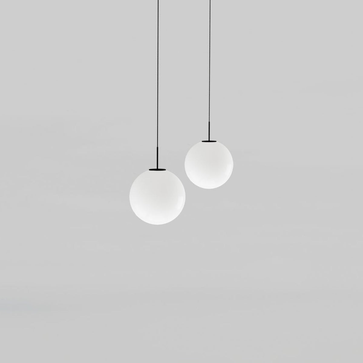 Mika Opal Glass Globe Pendant Light in Matt Black, two globe pendants of different sizes on black cables with matt black canopies, shown on a plain grey background.