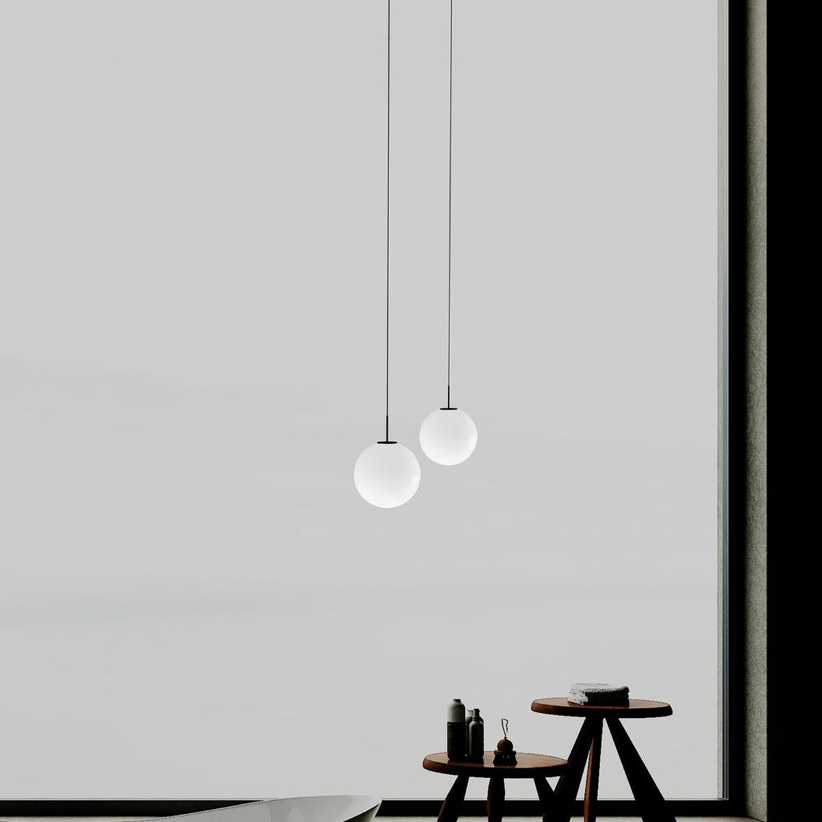 Mika Opal Glass Globe Pendant Light in matt black, two sizes shown on black cables above a wooden side table against a light grey wall.