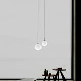 Mika Opal Glass Globe Pendant Light in matt black, two sizes shown on black cables above a wooden side table against a light grey wall.