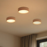 Three Bloom LED drum flush ceiling lights in ash wood with white diffusers, mounted on a beige bedroom ceiling near curtains and a window.