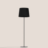 Kilma Ribbed Fabric Floor Lamp in matt black, featuring a pleated tapered fabric shade on a slim iron stem with round flat base, shown on a plain light background.