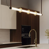 Roseline LED Ribbed Glass Linear Pendant Light in gold and brown, a long fluted glass bar with three gold discs, hung above a kitchen counter with brass tap.