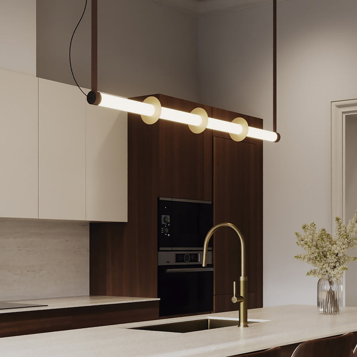 Roseline LED Ribbed Glass Linear Pendant Light in gold and brown, a long fluted glass bar with three gold discs, shown suspended above a kitchen island with warm white glow.