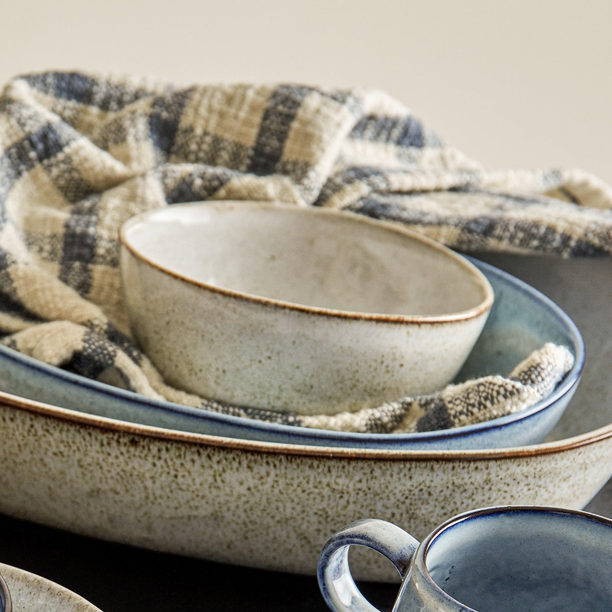 Sandrine Speckled Stoneware Bowl 15cm in grey, deep rounded sides with a dark rim line, shown with a matching serving dish and plaid cloth.