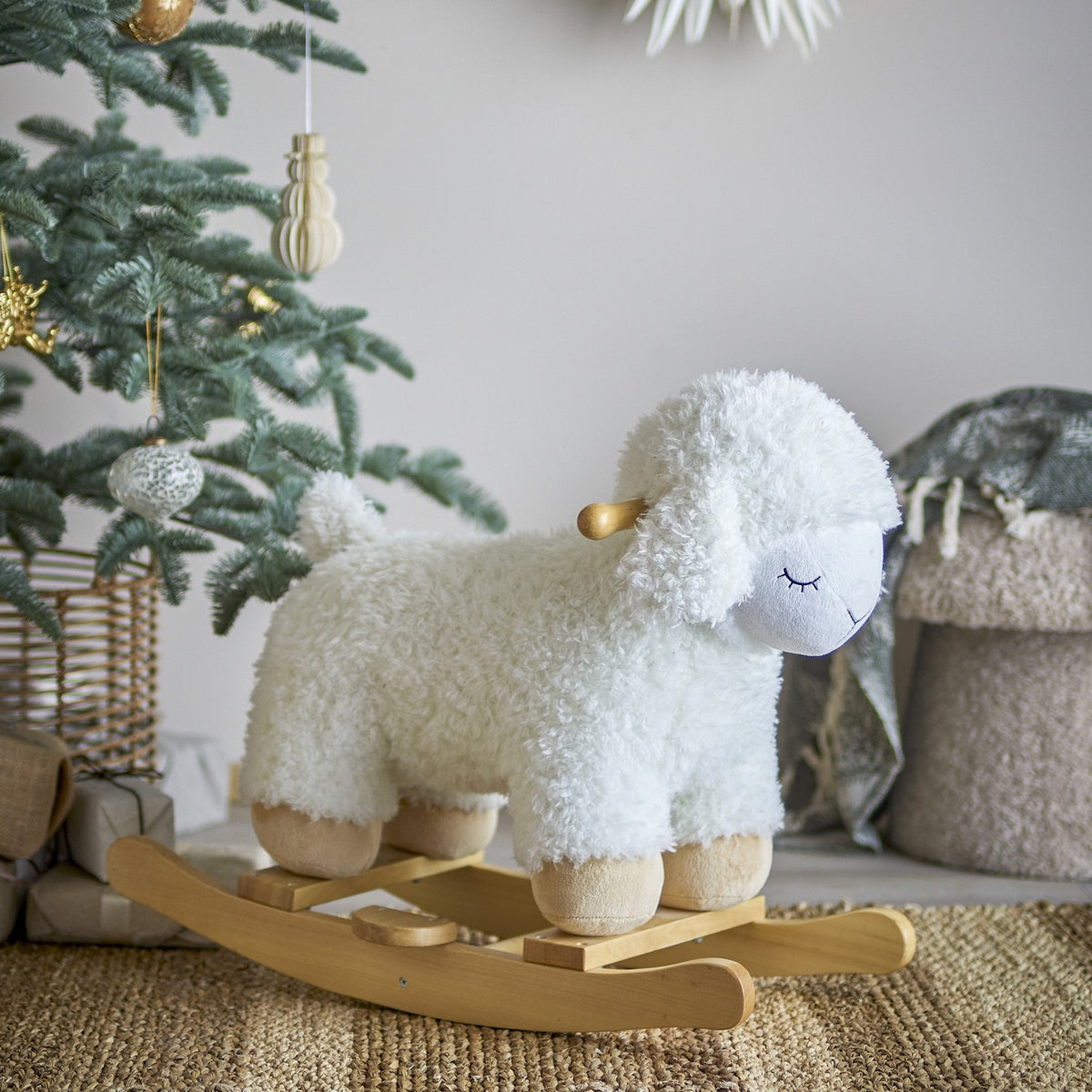Laasrith Rocking Sheep in white, a curly fabric ride-on toy with floppy ears, sleepy embroidered face and wooden handle, set on poplar wood rockers in a nursery scene beside a Christmas tree.