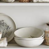 Bea Crackle Stoneware Deep Plates in cream, stacked on a shelf with an irregular rim, crackled finish, and a faint fern leaf motif, beside a matching patterned plate.