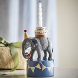 Flor Resin Candle Holder 18cm: elephant in a party hat carrying a two-tier cake and red ball, on a bunting-trimmed base with a lit twisted candle, beside a wrapped gift.