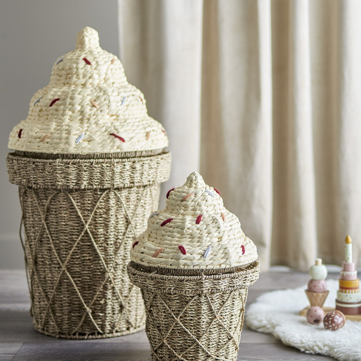 Cillie Seagrass Basket with Lid 72cm in Natural, cone-shaped with twisted base and stitched swirl lid, shown with a smaller matching basket in a nursery.