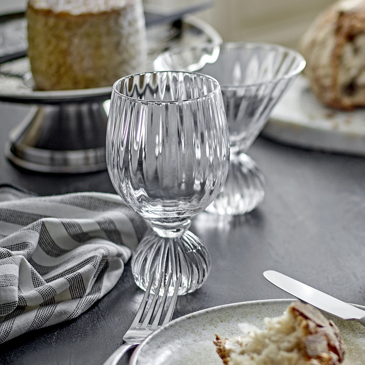 Taurin Round Wine Glass in clear ribbed glass with a short round foot, shown on a dining table beside bread and a striped napkin.