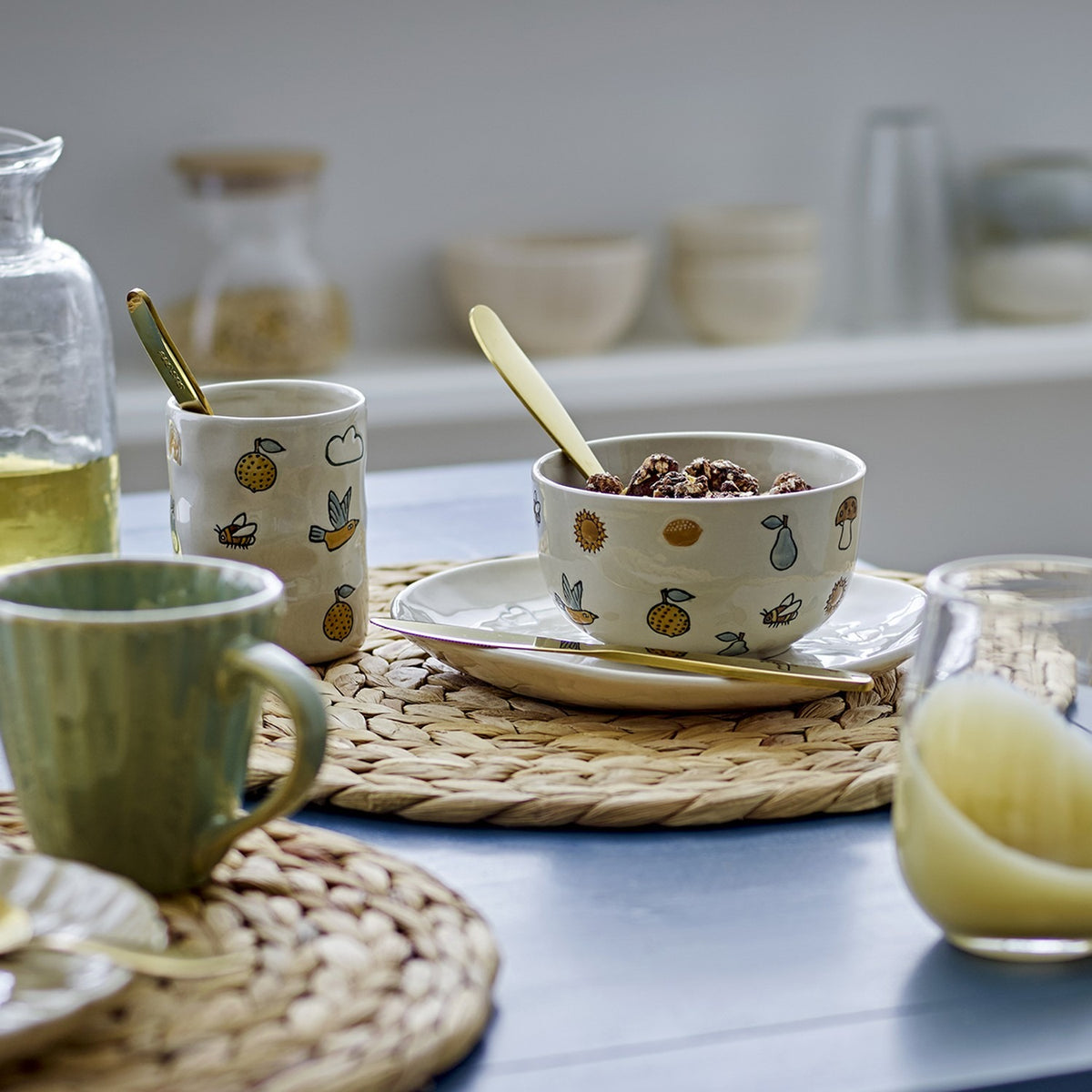 Agnes Stoneware Kids Dinner Set of 3 in cream, patterned plate, bowl and cup with fruit and nature motifs, shown on a table with gold cutlery and woven mats.