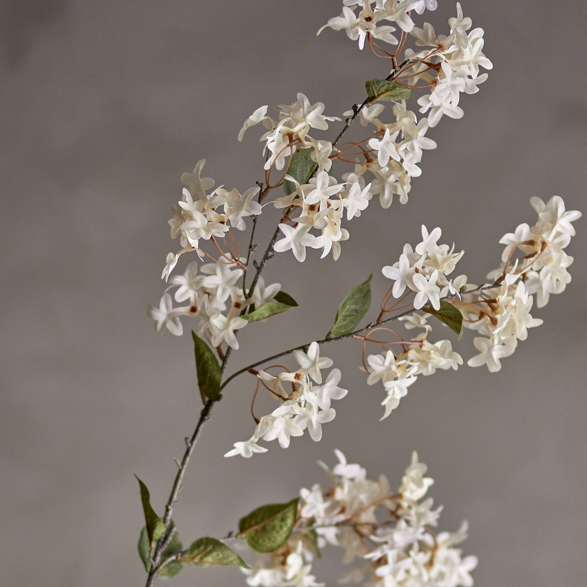 Artificial myrtle stem in white with clusters of small star-shaped flowers and rounded green leaves along slender branches, set against a plain grey background.