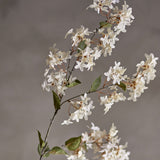 Artificial myrtle stem in white with clusters of small star-shaped flowers and rounded green leaves along slender branches, set against a plain grey background.