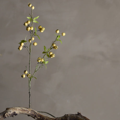 Hawthorn Artificial Branch in yellow, a slender faux stem with clustered round berries and small pointed leaves, set in driftwood against a plain grey background.