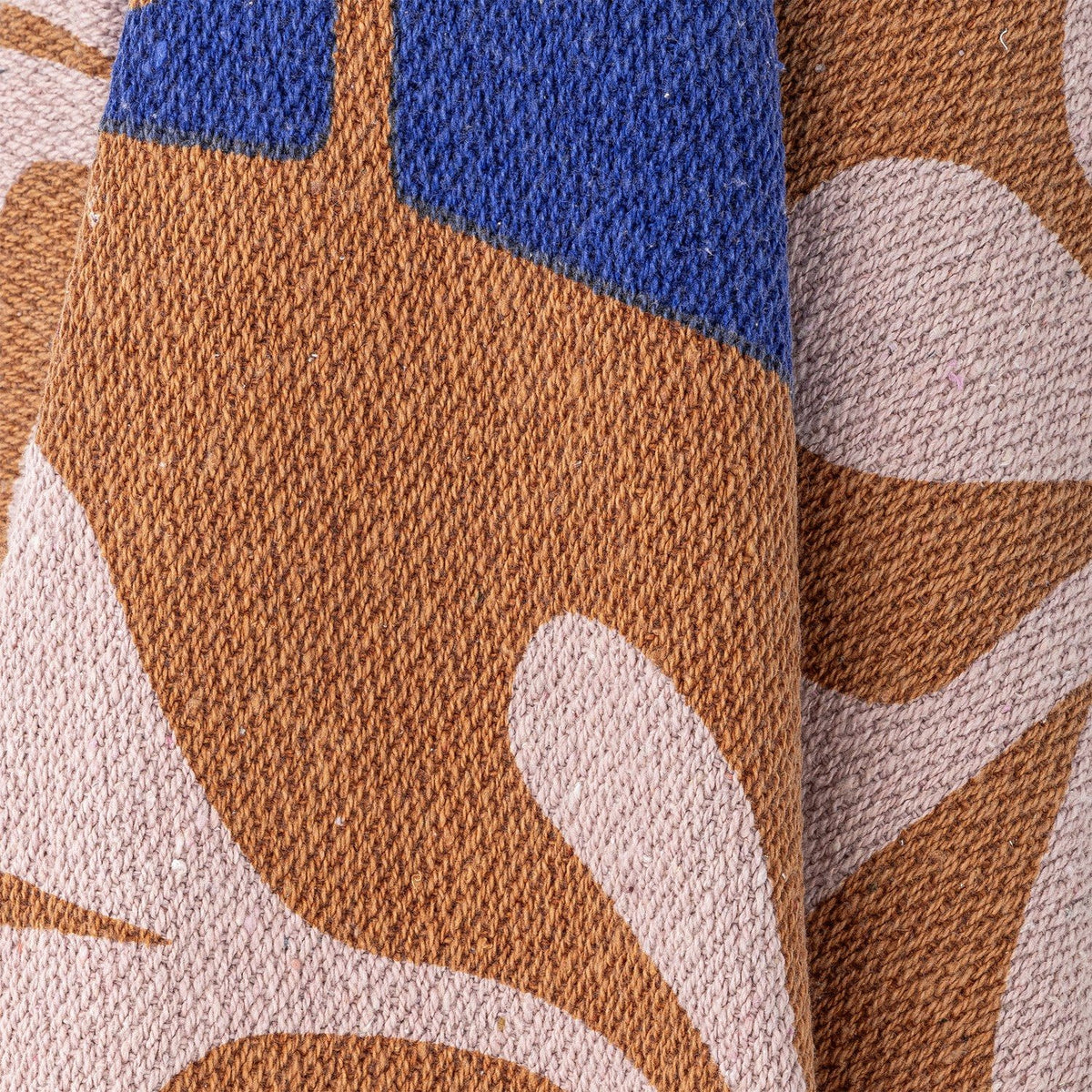 Close-up of the Atle Leaf Cotton Throw in brown, showing woven cotton fabric with large rounded leaf shapes in blue and dusty pink.