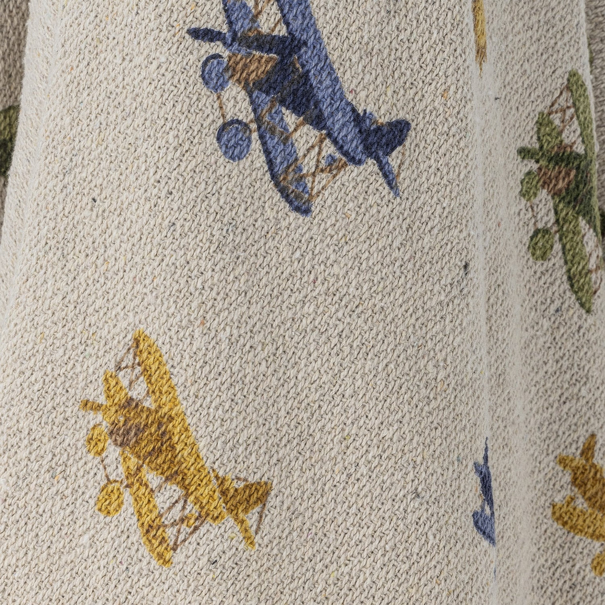Close-up of the Plane Cotton Throw in beige, showing a woven cotton knit fabric printed with blue, green, and yellow biplane motifs.