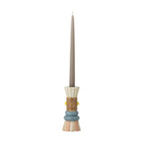Minio Ceramic Vase styled as a candle holder base, shaped like a tiered figure in cream, tan, blue, and pink tones, holding a tall grey taper candle on a plain white background.