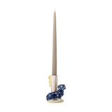 Stoneware candle holder shaped like a seated navy polka-dot dachshund beside a striped cylindrical holder with a scalloped fin, holding a tall grey taper candle.