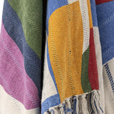 Close-up of the Artista Cotton Throw in multicoloured abstract shapes, showing a woven texture in mustard, blue, green, pink, and red with knotted fringe tassels.