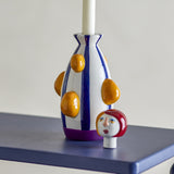 Conneli Ceramic Candle Holder in Multi, a dolomite bottle-shaped holder with blue stripes and raised orange bumps, its detachable painted head figure placed beside it on a blue shelf.