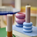 Tana Speckled Candle Holders in stacked stoneware with ribbed blue and pink bases, holding tall pillar candles on a book in a softly lit room.