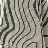 Close-up of the Woodsby Striped Cotton Throw in natural cotton with wavy green stripes resembling wood grain, showing the textured woven fabric and folded edge.