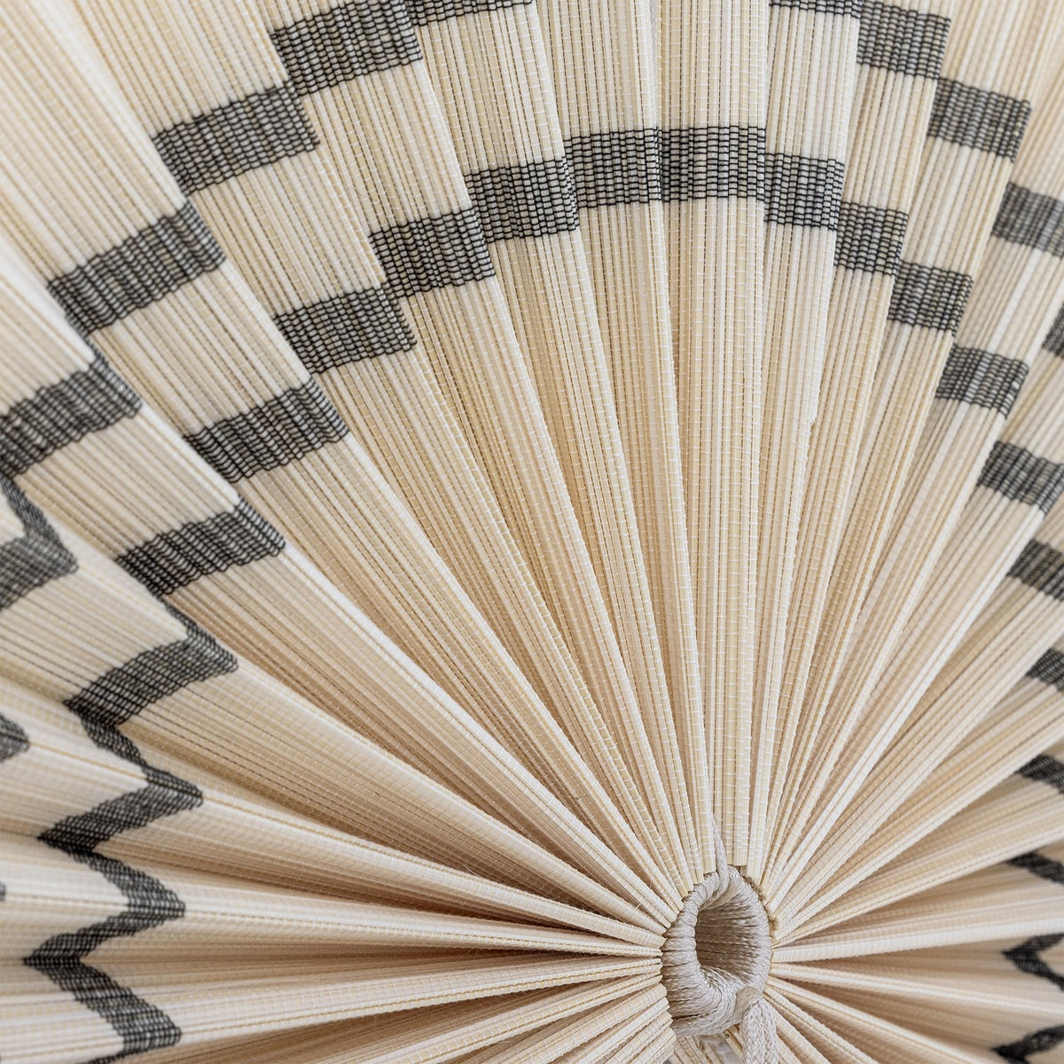 Close-up of the Jaime Bamboo Wall Decor 70cm pleated fan in natural bamboo, showing fine radiating slats with contrasting zigzag bands and the central cord loop.