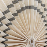 Close-up of the Jaime Bamboo Wall Decor 70cm pleated fan in natural bamboo, showing fine radiating slats with contrasting zigzag bands and the central cord loop.