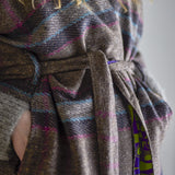 Close-up of the Rieti Striped Kimono in grey, showing the woven tie belt and striped fabric with pink and blue accents, reverse side revealing a green and purple geometric print.