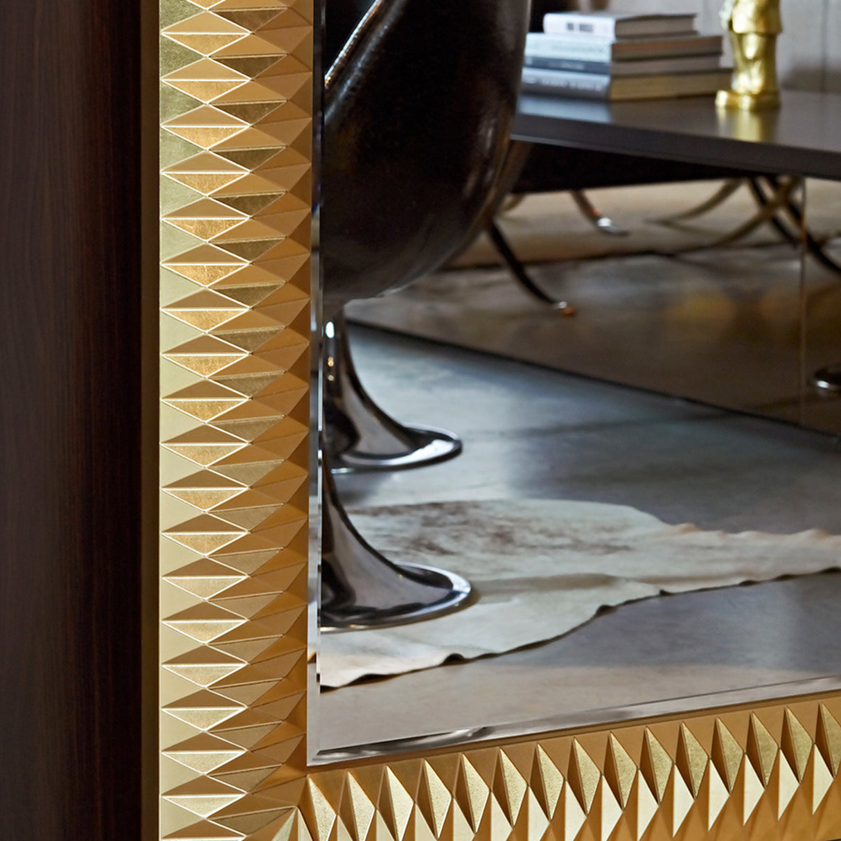 Close-up of the faceted gold surround with the glass reflecting a cowhide rug and dark timber furniture behind the camera.
