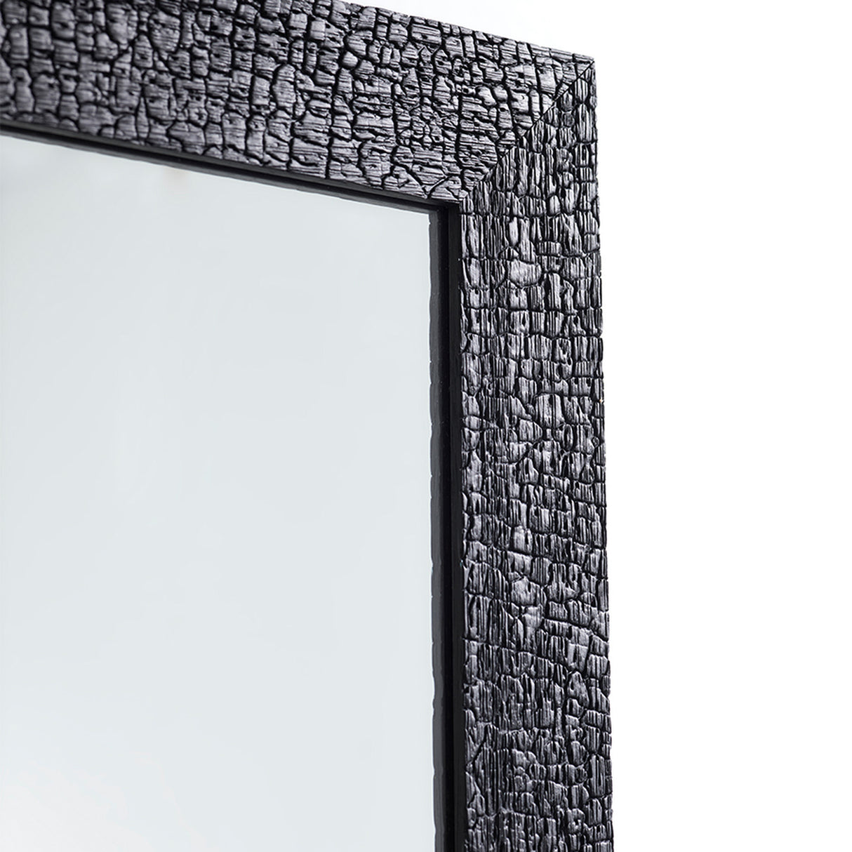 Close-up of the charred black frame at an angle, the crackled surface running the length of the timber edge.