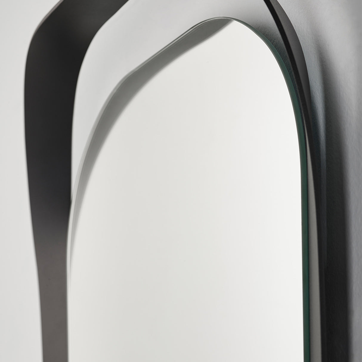 Close-up of the top curve, the black frame turning away from the wall as it rises around the oval glass.