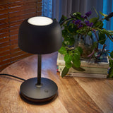 Bol M/37 Dome LED Table Lamp in matte black, dome shade on slim stem with round weighted base and touch dimmer, shown on a wooden table beside books and a plant.