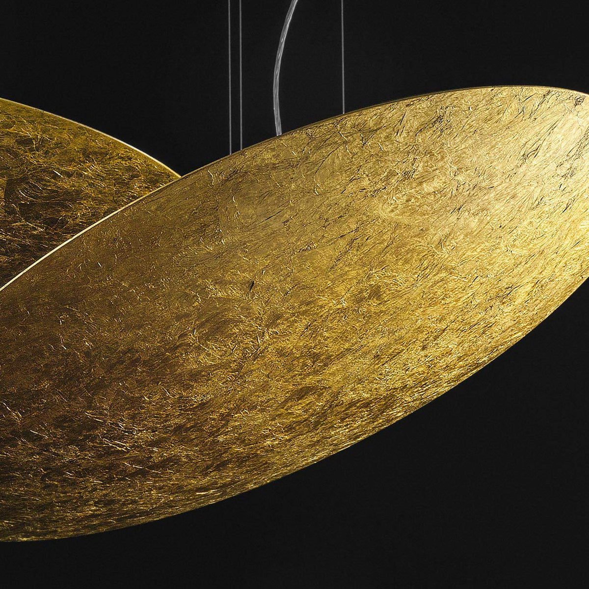 Close-up of the Gong Aluminium Disc LED Pendant Light 60cm, showing its shallow gold leaf finish disc with a textured metallic surface, suspended on fine wires against a black background.