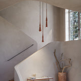 Slend 02 Aluminium Pendant Light in textured terracotta, slim tapering body with ringed detail, shown over a staircase landing in a modern interior.