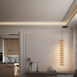 Yuyun S/9L pendant light with nine stacked woven beige cotton shades on a slim rod, integrated LED, shown illuminated beside a panelled wall in a living room setting.