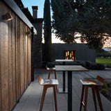 Nut A/01 Stainless Steel LED outdoor wall lights with rounded, bell-shaped heads mounted on a timber-clad exterior wall, illuminating an outdoor seating area at dusk.