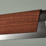 Close-up of the Roof S160 LED pendant light showing its wood-finish folded cover curving over a ribbed black and brushed metal underside, against a plain grey background.