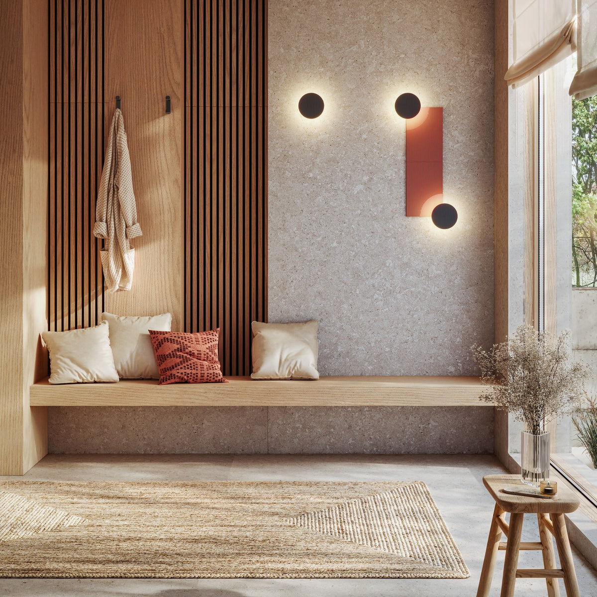 Arid A/01 round aluminium LED wall lights in textured graphite brown, shown mounted in a set of three on a stone wall above a wooden hallway bench, glowing with warm backlit rings.