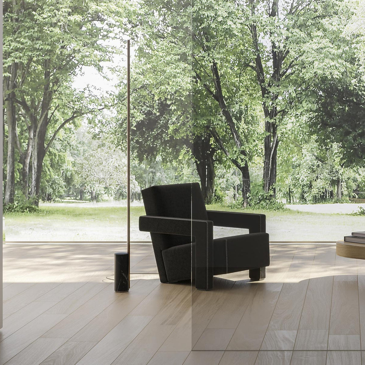 Hilow Line Nero Marquina linear floor lamp with slim brushed brass rod and black, white-veined marble cylindrical base, shown beside a black armchair in a sunlit room.