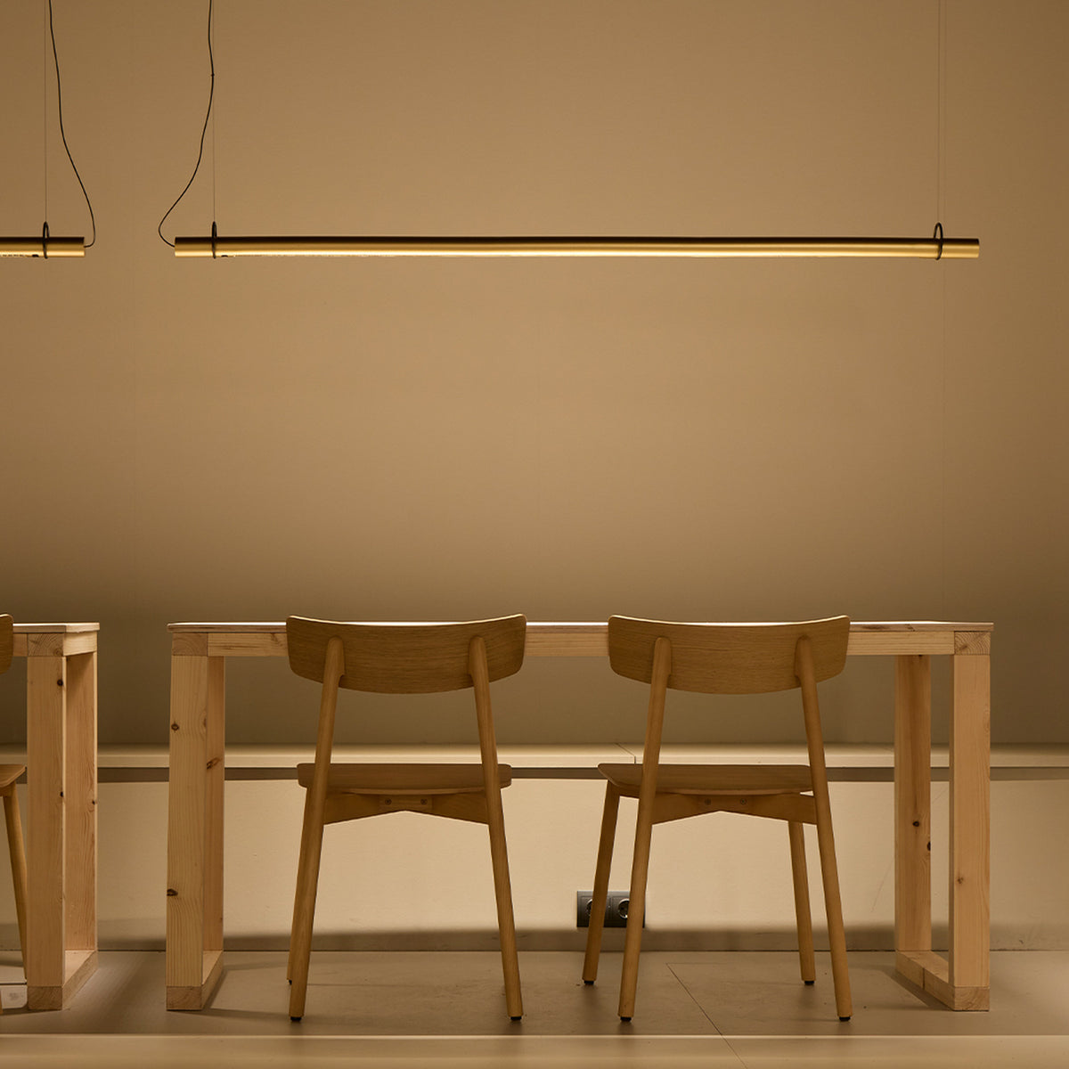 Solid SH 160 Cylinder LED Pendant Light in black, a slim horizontal tube suspended above a wooden dining table with chairs in a warm-toned room.