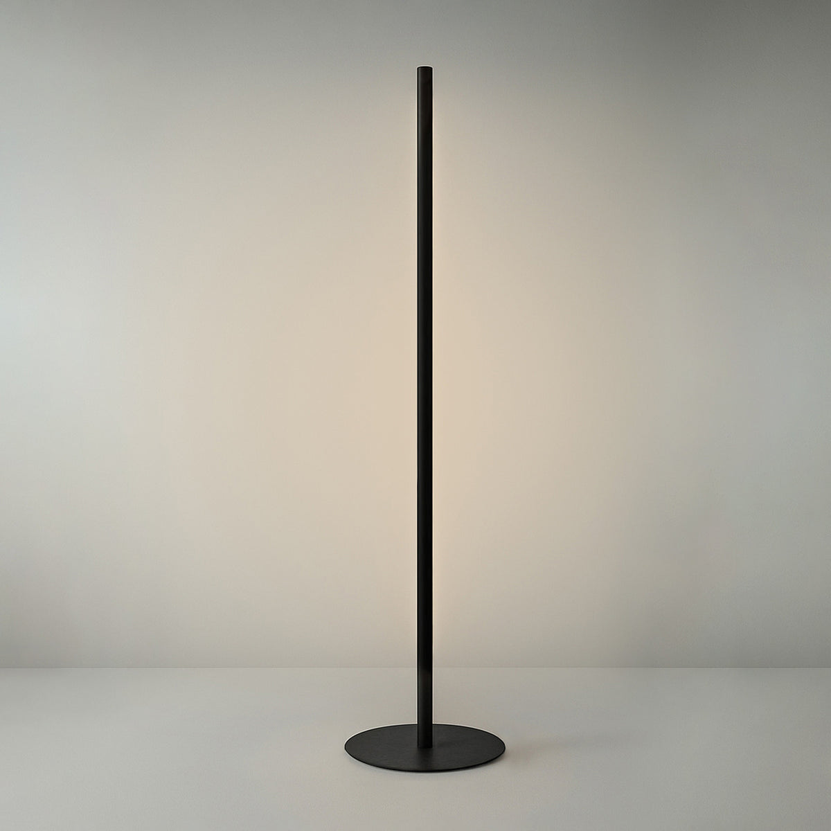 Solid F 240 Cylinder LED Floor Lamp in matte black, a slim upright stem on a round disc base with a long illuminated line of warm white light, shown against a plain light grey background.