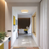 Plafonet 60 Ribbon LED ceiling light with pleated white drum shade, shown flush-mounted in a hallway with warm wood panelling and white decor.