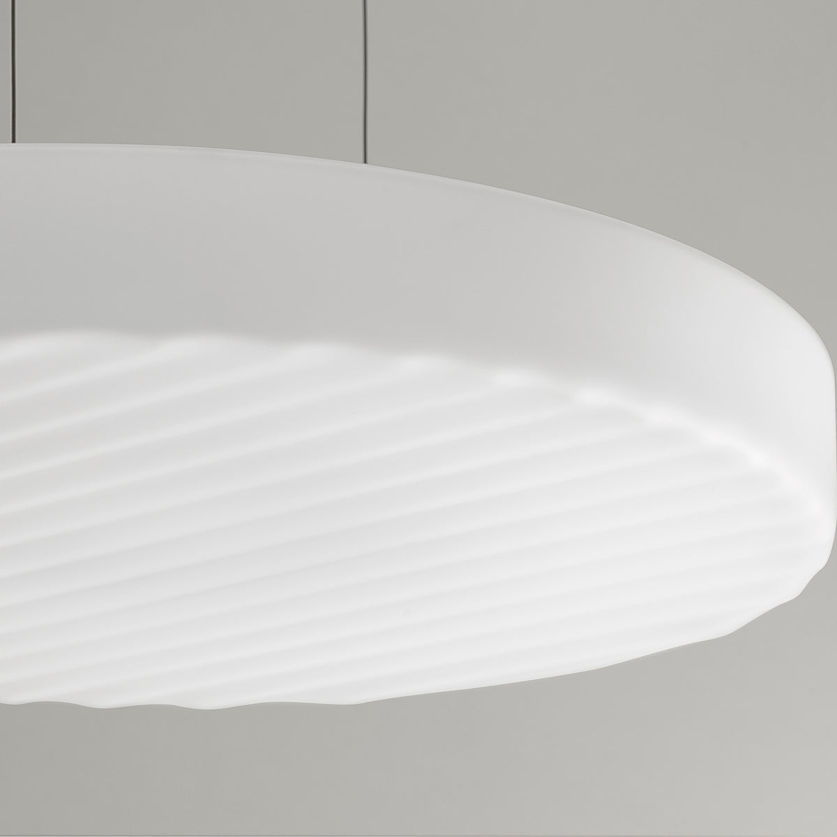 Close-up of the Côte LED pendant light, a broad shallow disc of frosted white glass with fine diagonal ribbing on its underside, shown against a plain light grey background.