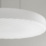 Close-up of the Côte LED pendant light, a broad shallow disc of frosted white glass with fine diagonal ribbing on its underside, shown against a plain light grey background.
