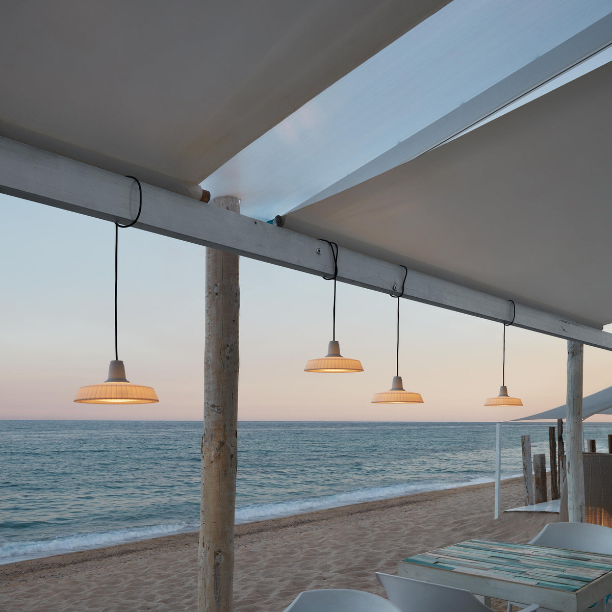 Marietta S/32 Dome LED Outdoor Pendant Lights in white with pleated dome shades on black cables, shown hanging from a beach pavilion beam at dusk.