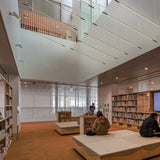 BIMU S200 Uni linear LED pendant lights in black, slim bar fixtures suspended from cables, shown installed above a library lounge with seating and bookshelves.