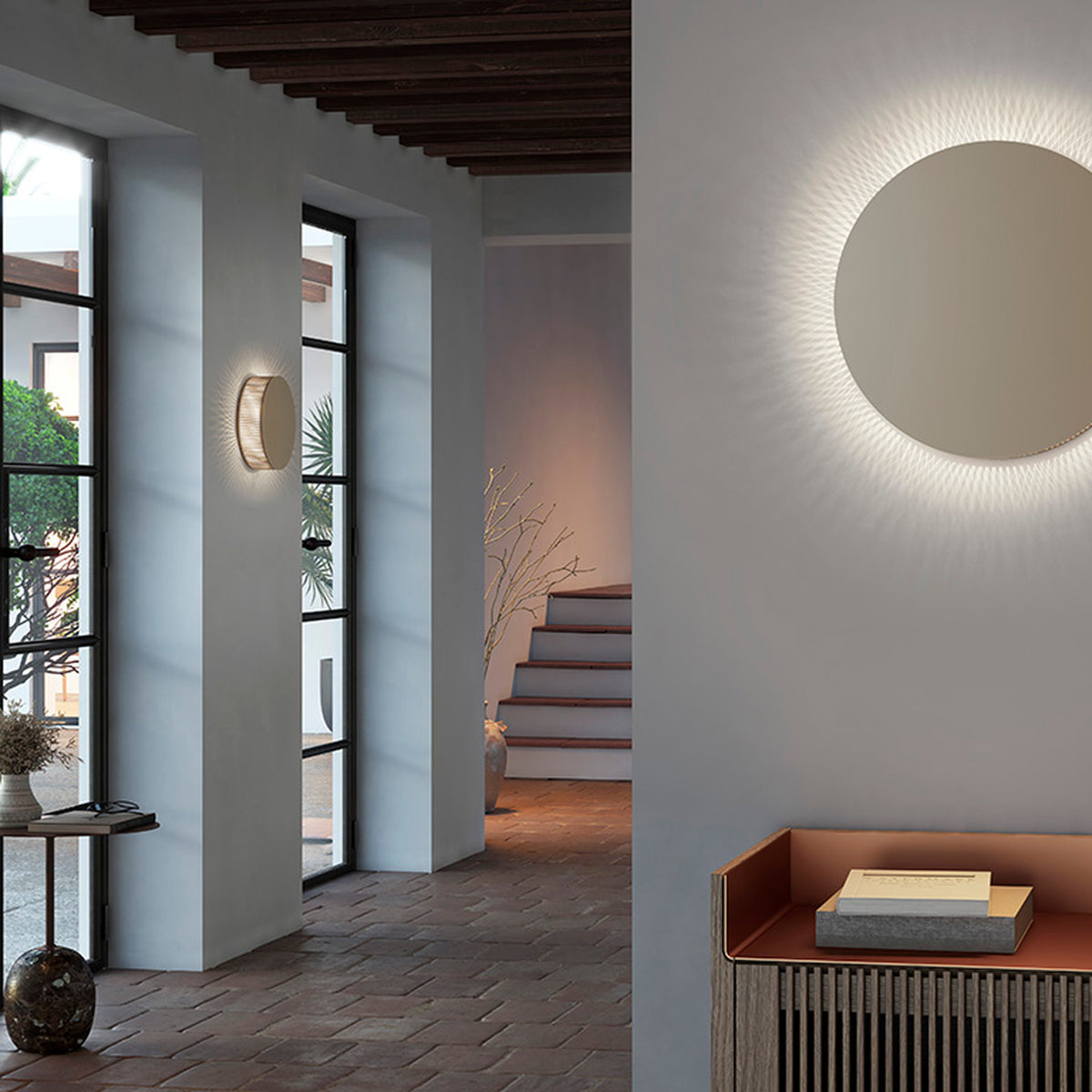 Helios A/02 round LED wall light in Oak Brown & Beige fabric finish, shown glowing softly on a hallway wall and as a backlit disc beside an entryway console.